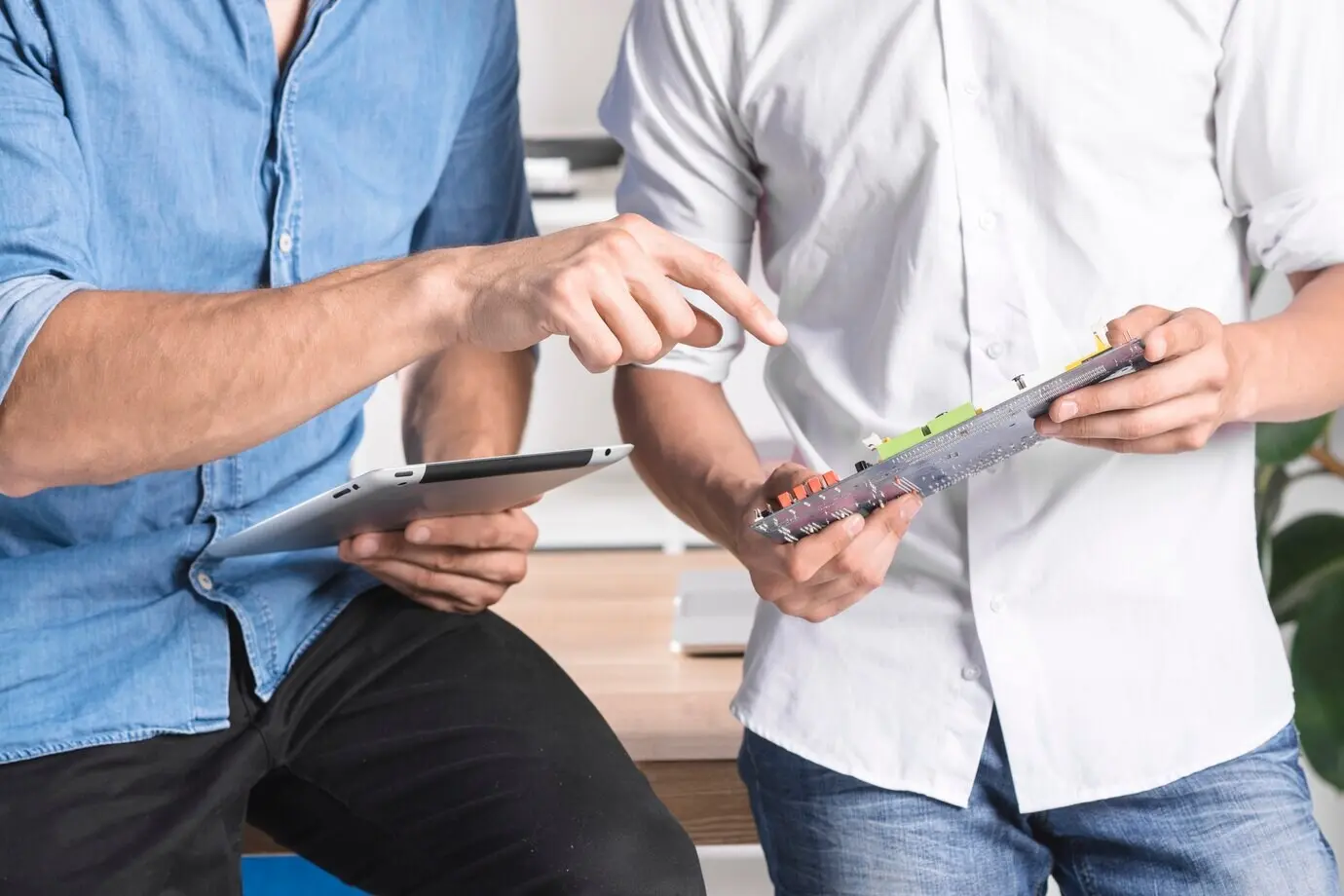 Ein Mann assistiert einem männlichen Techniker, der ein Computer-Motherboard hält.